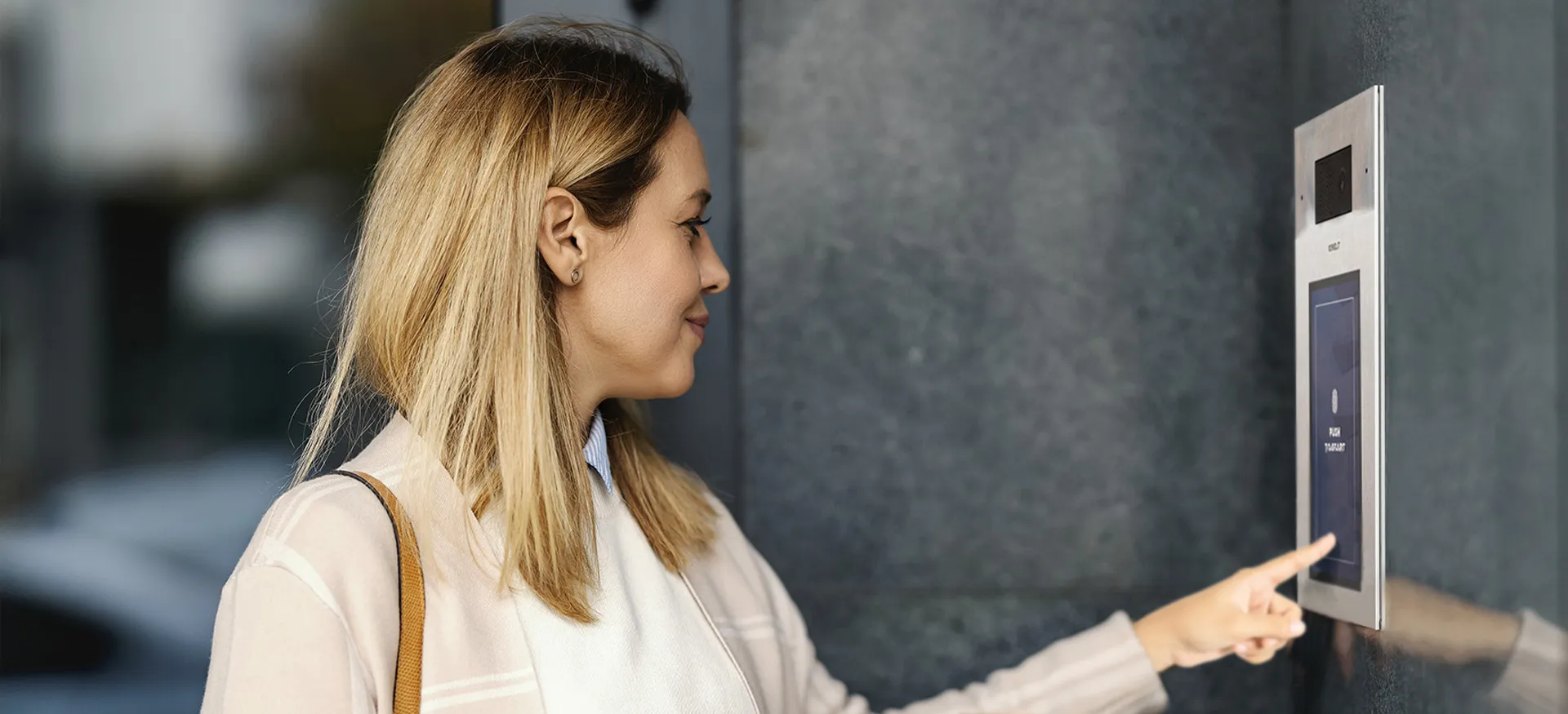 Donna che utilizza un pannello esterno di un moderno sistema di videocitofonia in un contesto commerciale/uffici.