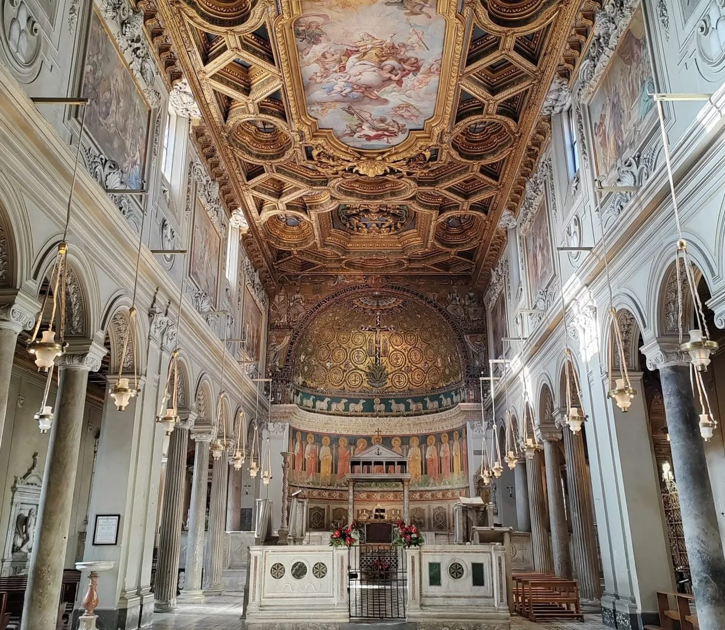 Interno della Basilica di San Clemente a Roma con soffitto dorato e mosaici.