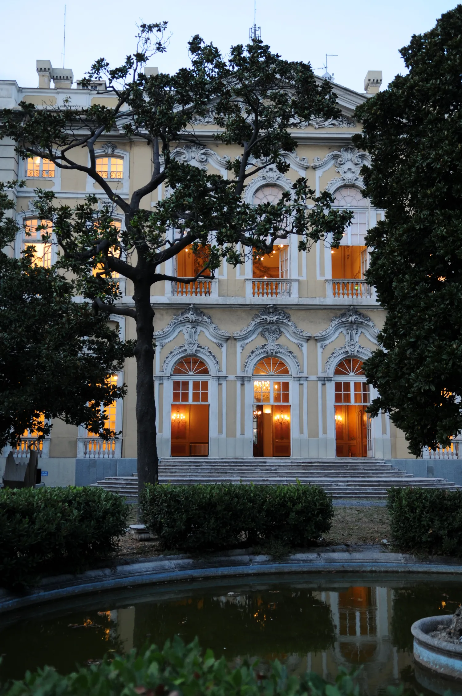 Facciata di Villa Bombrini al tramonto con saloni illuminati e vasca del giardino