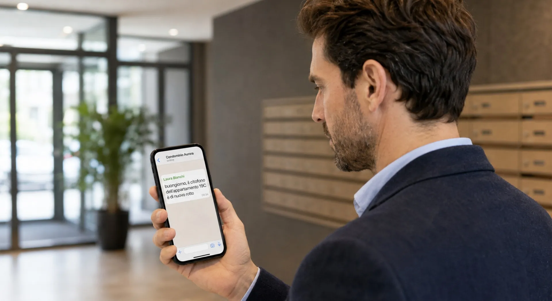 Amministratore di condominio legge su smartphone la segnalazione di un citofono condominiale rotto
