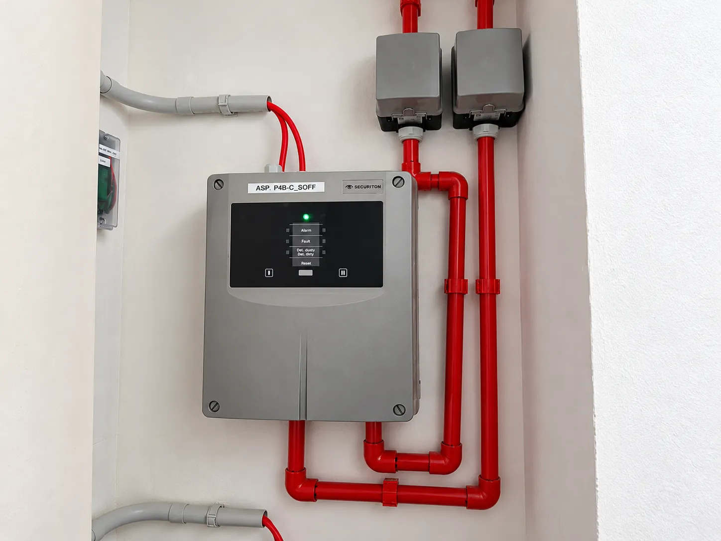 Rivelatore di fumo ad aspirazione Securiton con tubazioni rosse di campionamento installato a parete