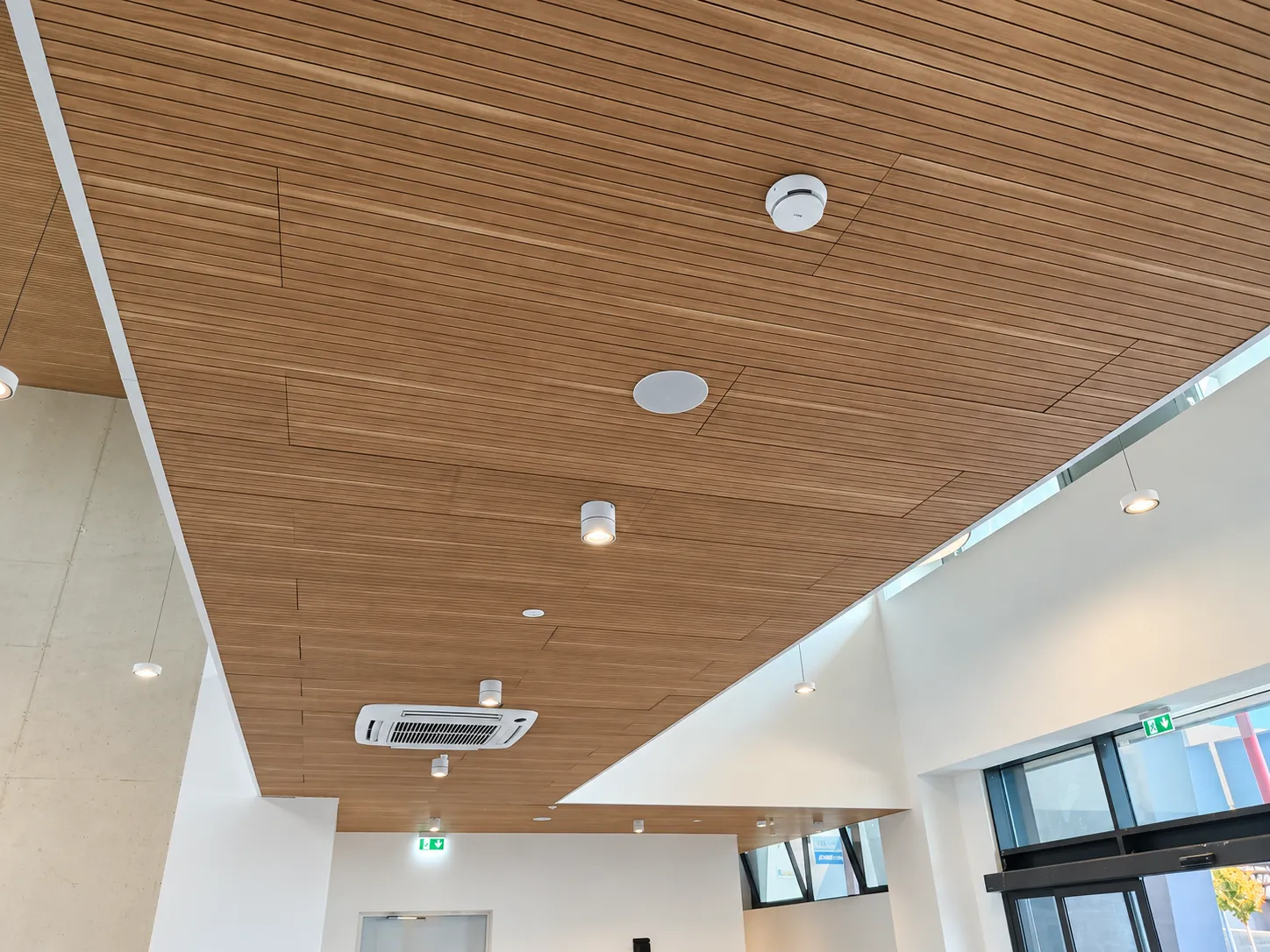 Rivelatore di fumo e diffusore sonoro EVAC installati su un controsoffitto in legno nella hall di un edificio